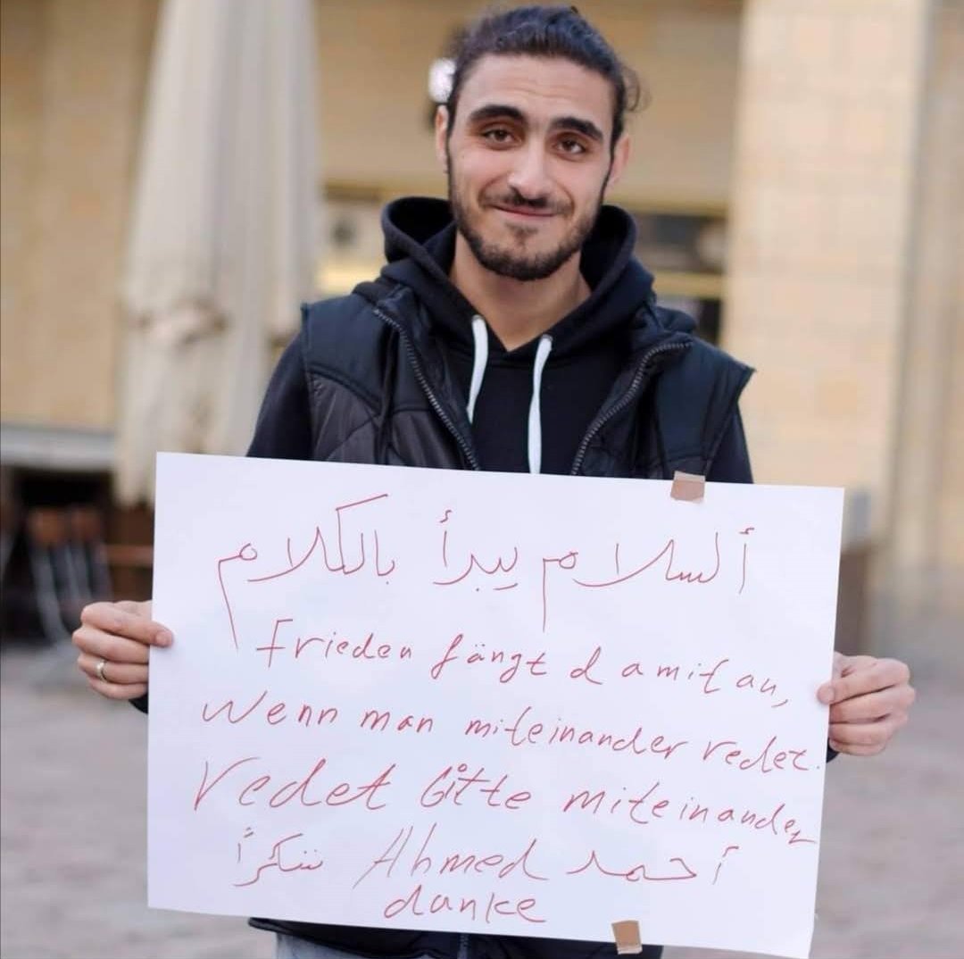 Ahmed Béjaoui hält ein Schild: Frieden fängt damit an, wenn man miteinander redet.